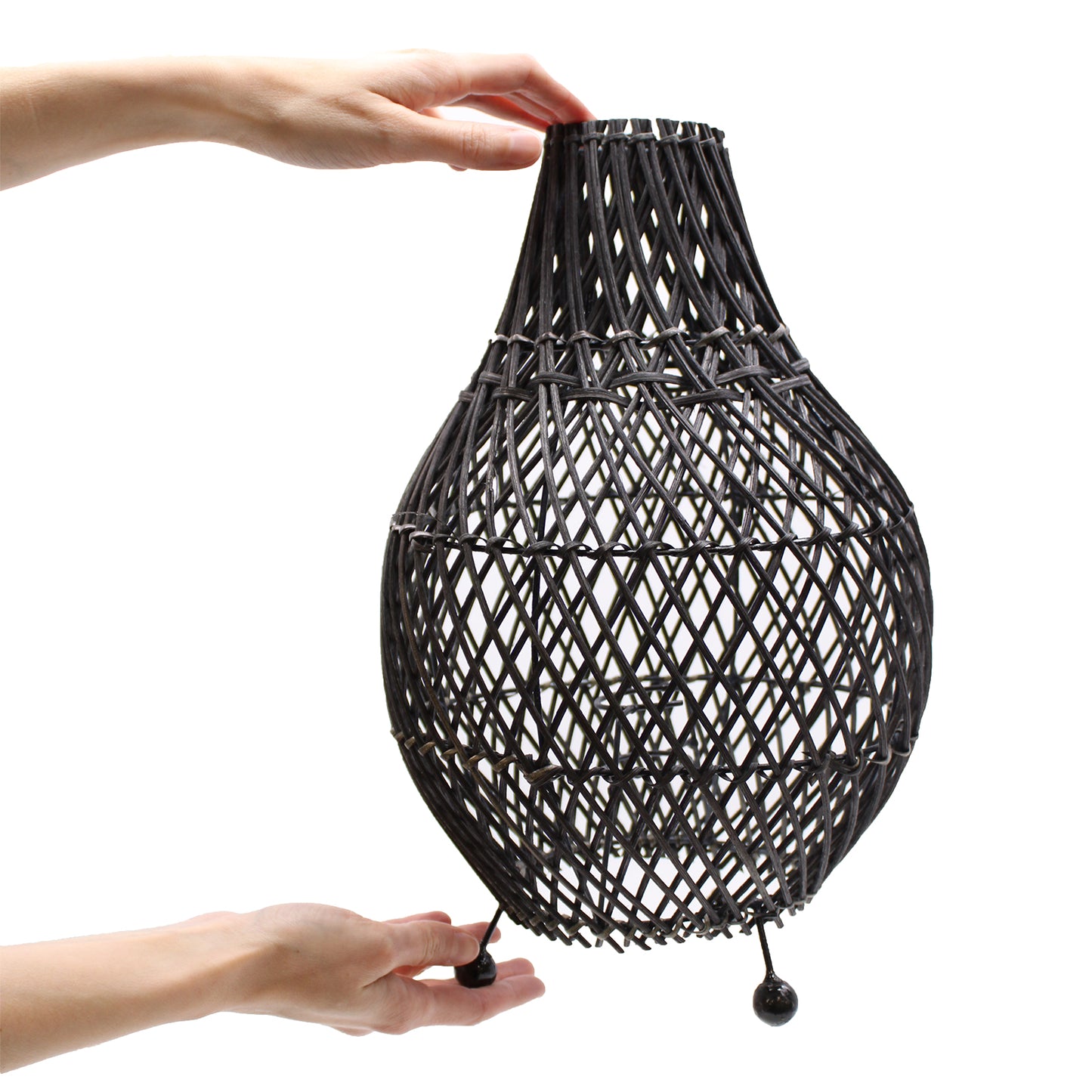 Dark rattan lamp being held to show scale and organic craftsmanship, suitable for earthy home decor.