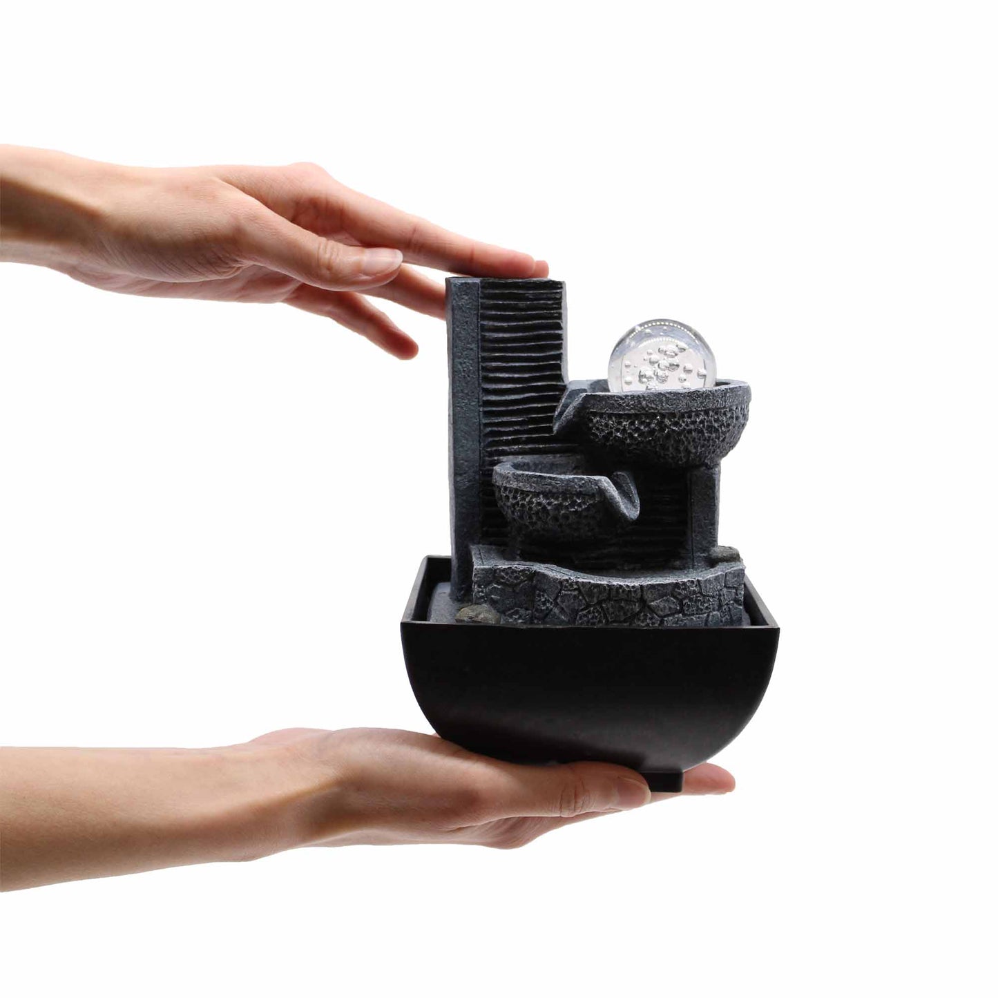 Hands holding compact indoor tabletop fountain with flowing water feature and orb