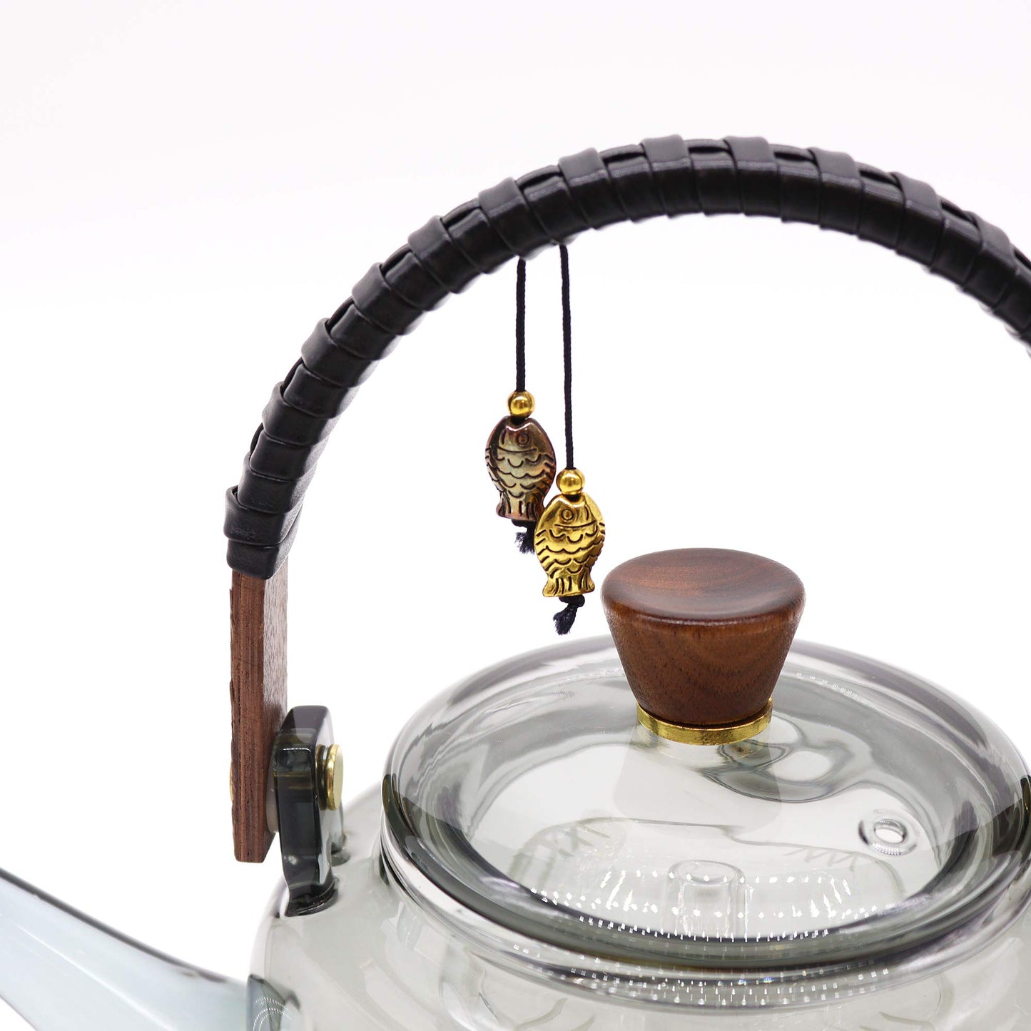 Close-up of curved wooden handle with black wrap and fish charms on glass teapot