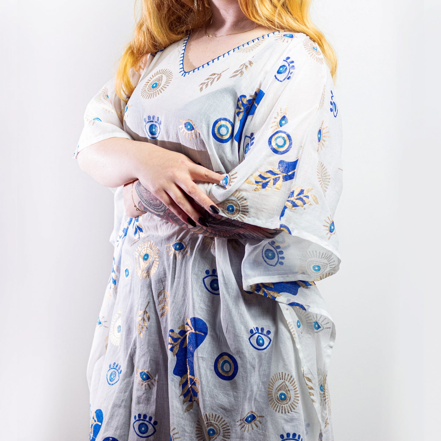 Woman wearing white cotton kaftan with blue and gold evil eye pattern, relaxed beachwear fit