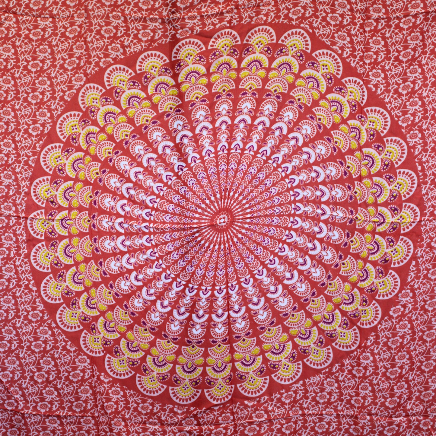Laid flat sarong displaying circular peacock-style mandala in vibrant orange, pink, and green tones