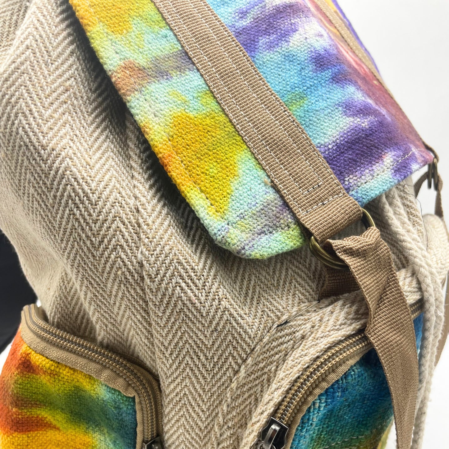 Close-up of colorful tie-dye flap and sturdy brown straps on eco-friendly hemp backpack with artisan stitching