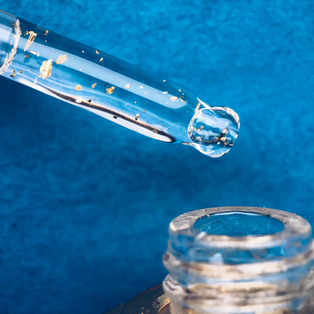 Glass dropper with a drop of liquid over a container on a blue background