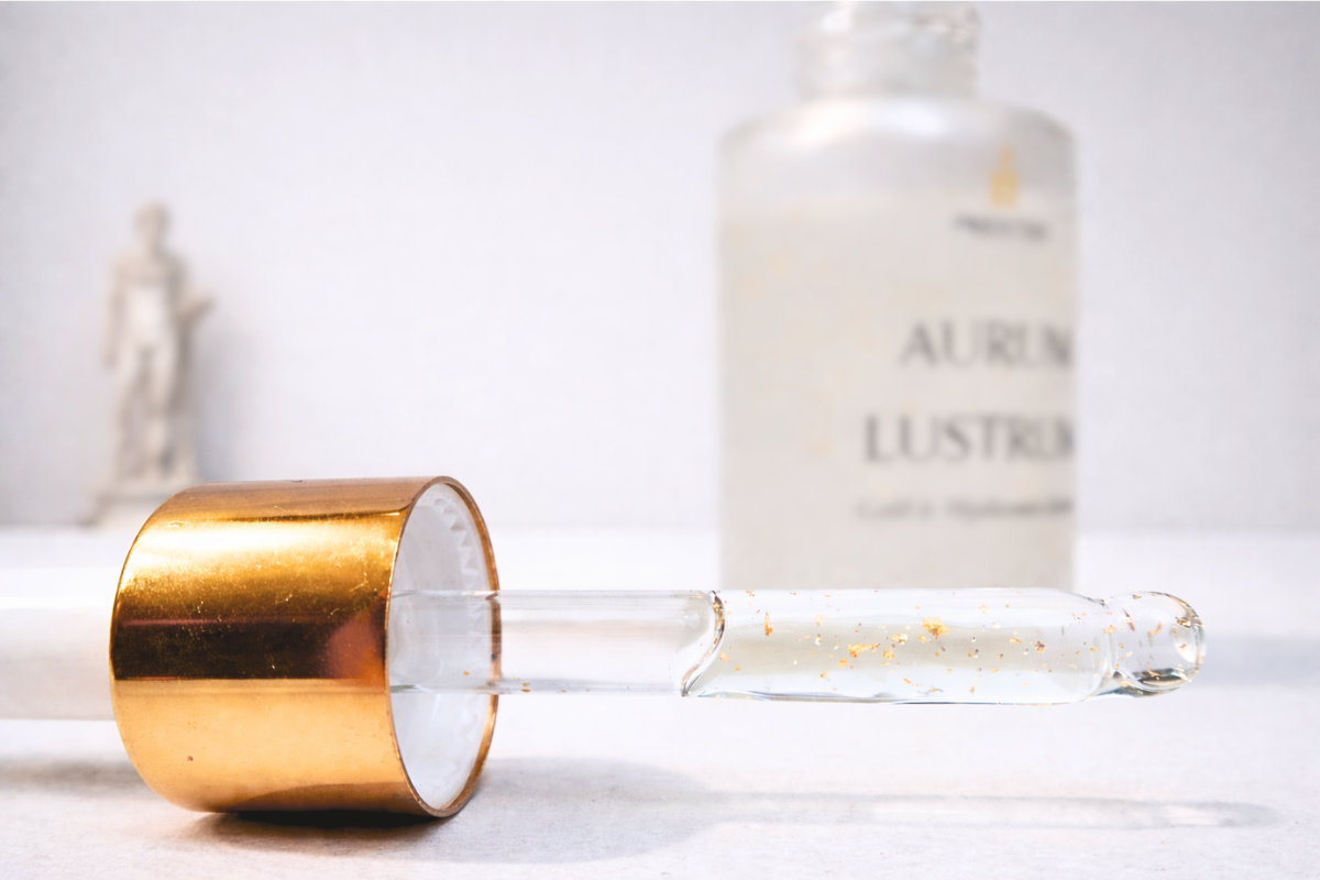 Gold-tipped dropper bottle with a white bottle labeled 'Aurum Lustrum' on a light background