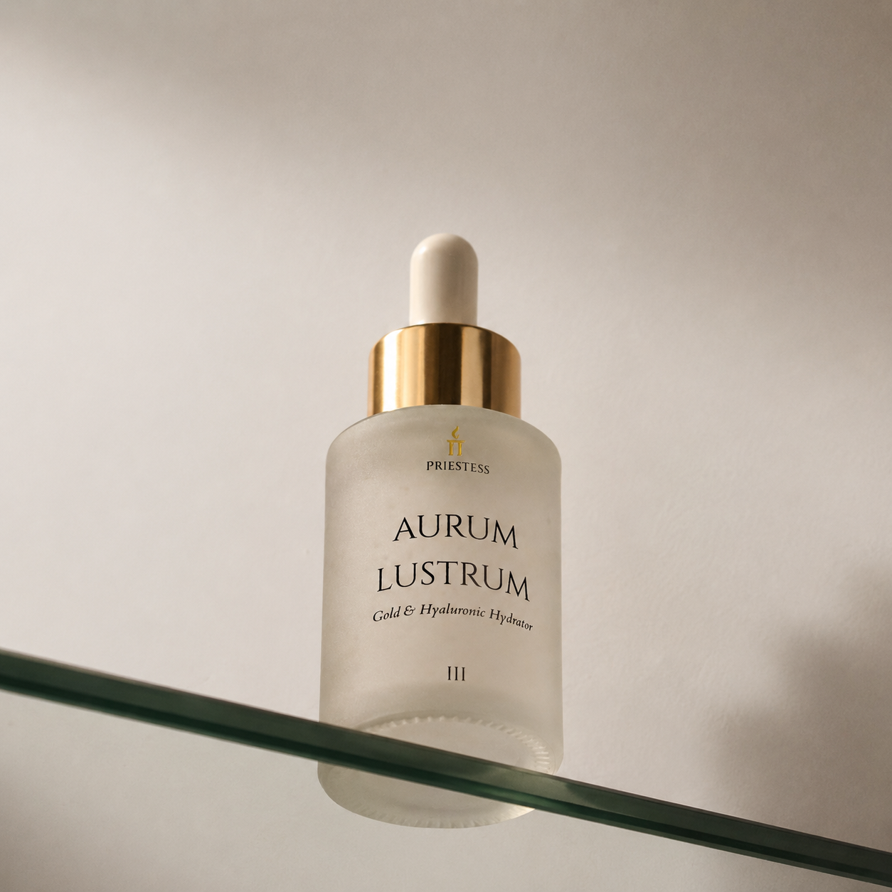 Priestess Aurum Lustrum Cold & Hyaluronic Hydration serum in a frosted glass dropper bottle with a gold collar and white dropper cap, resting on a glass shelf against a neutral background.