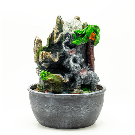 Tabletop water fountain featuring two elephants and a palm tree, with cascading water and a tropical mountain design in a grey resin bowl.