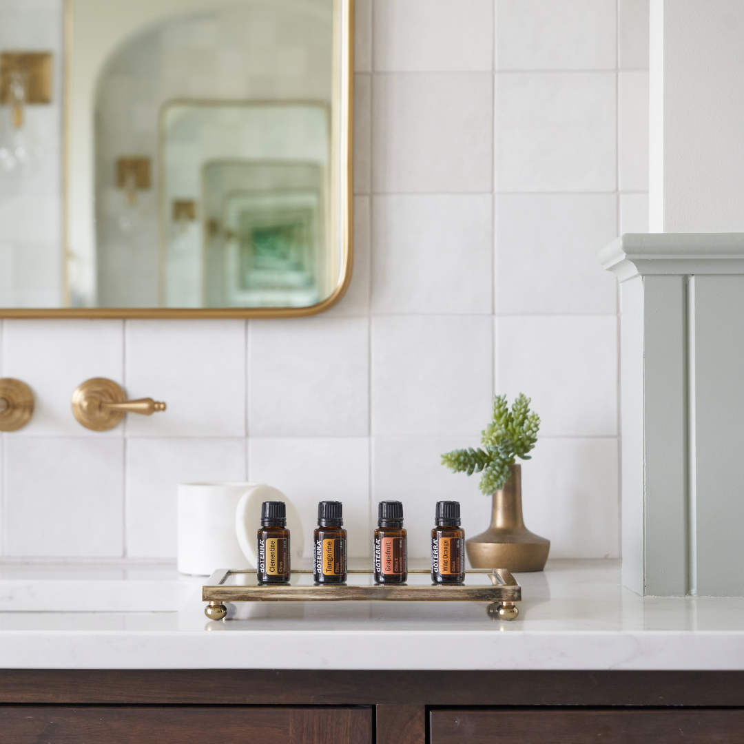 Bathroom scene with several amber essential oil bottles neatly arranged on a white counter beside a plant and mirror, styled for a modern wellness or skincare setting.