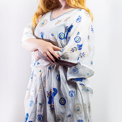 Woman wearing white cotton kaftan with blue and gold evil eye pattern, relaxed beachwear fit