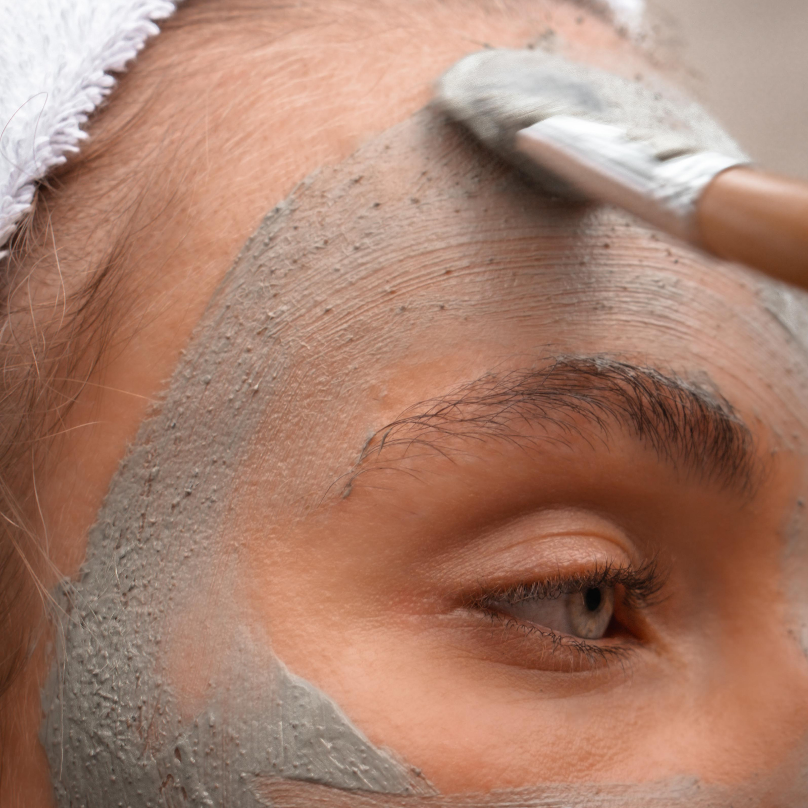Person applying a gray facial mask to their face with a brush.