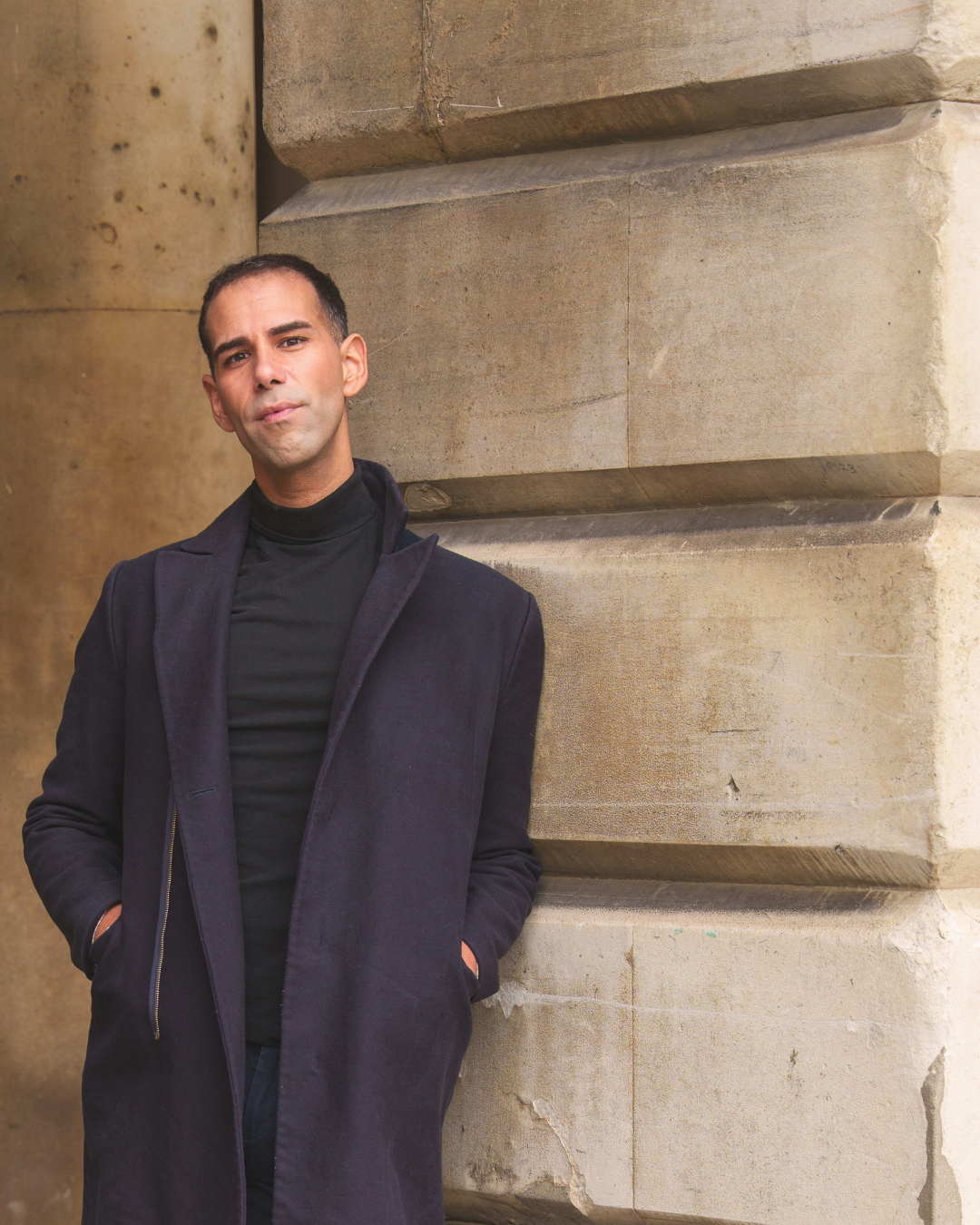 Man in a dark coat standing against a stone wall
