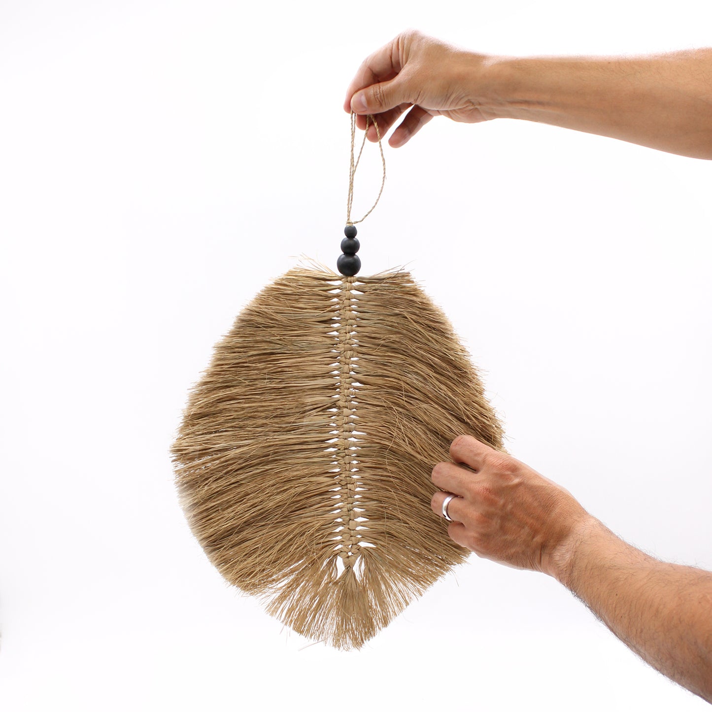 Raffa leaf wall decor held by hand to show scale, featuring natural fibers and handcrafted pinewood bead detail.