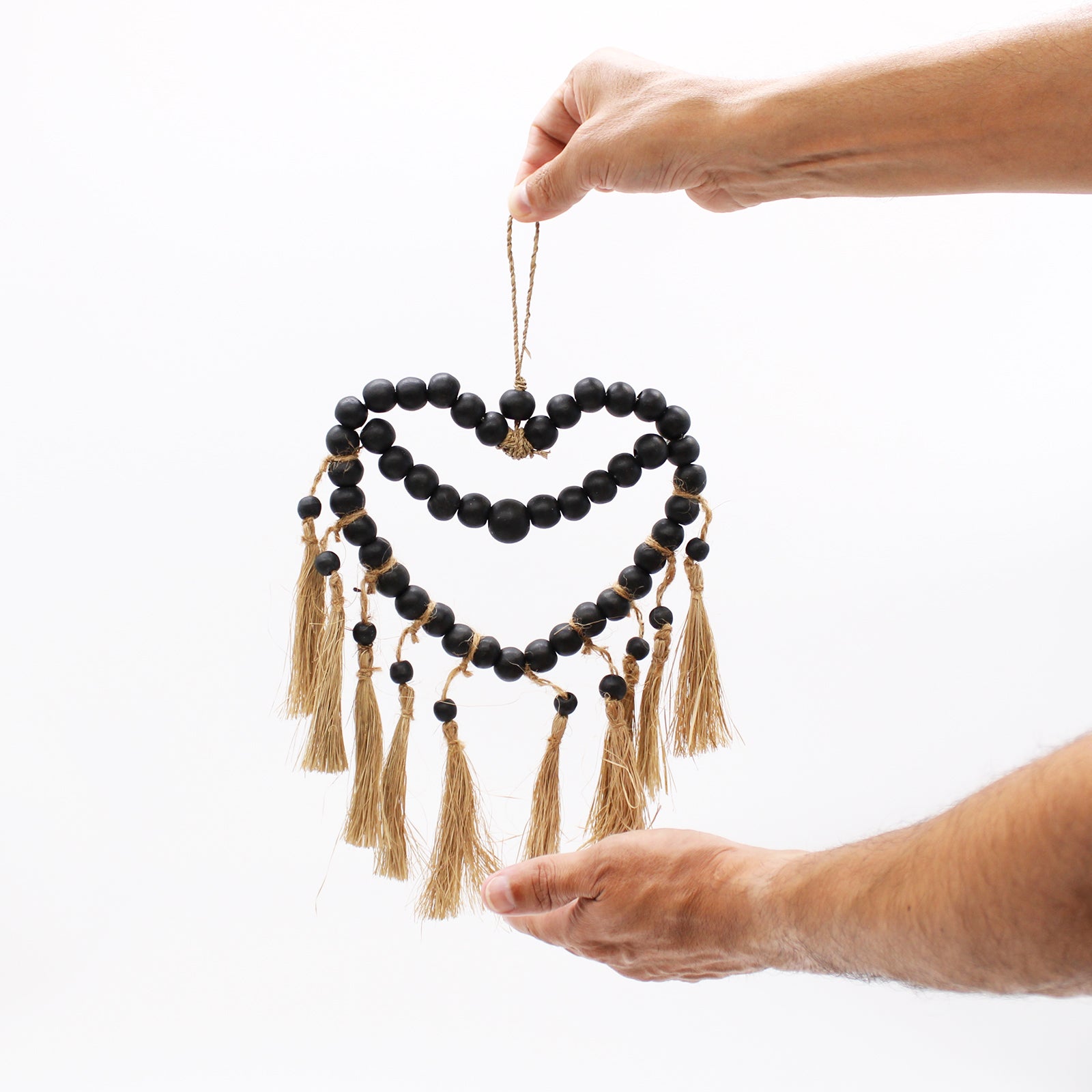 Small wooden beaded heart mobile held up against a white wall, showing size and delicate handmade construction.