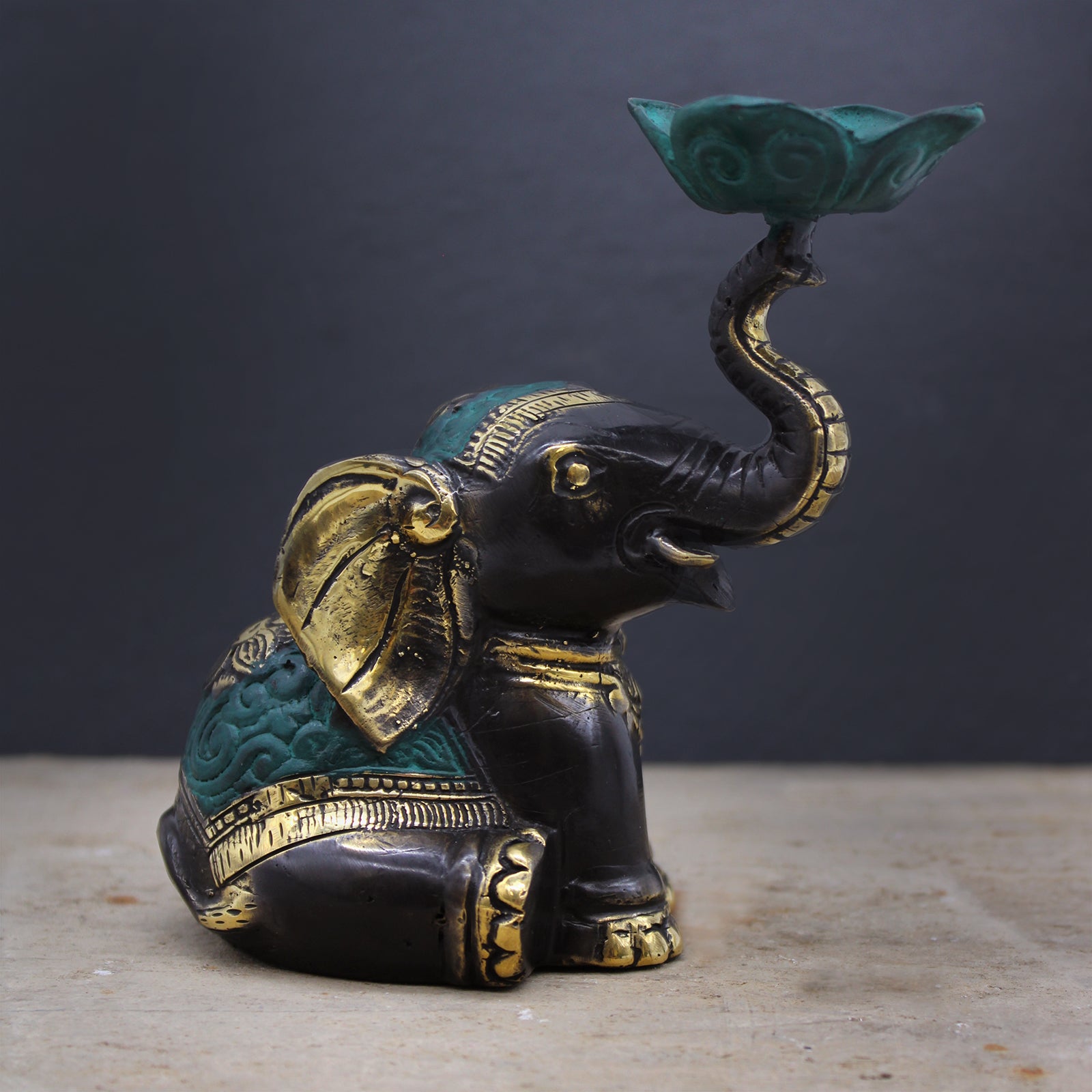 Brass elephant candle holder with green lotus dish shown on stone surface against dark grey background, spiritual decor accessory