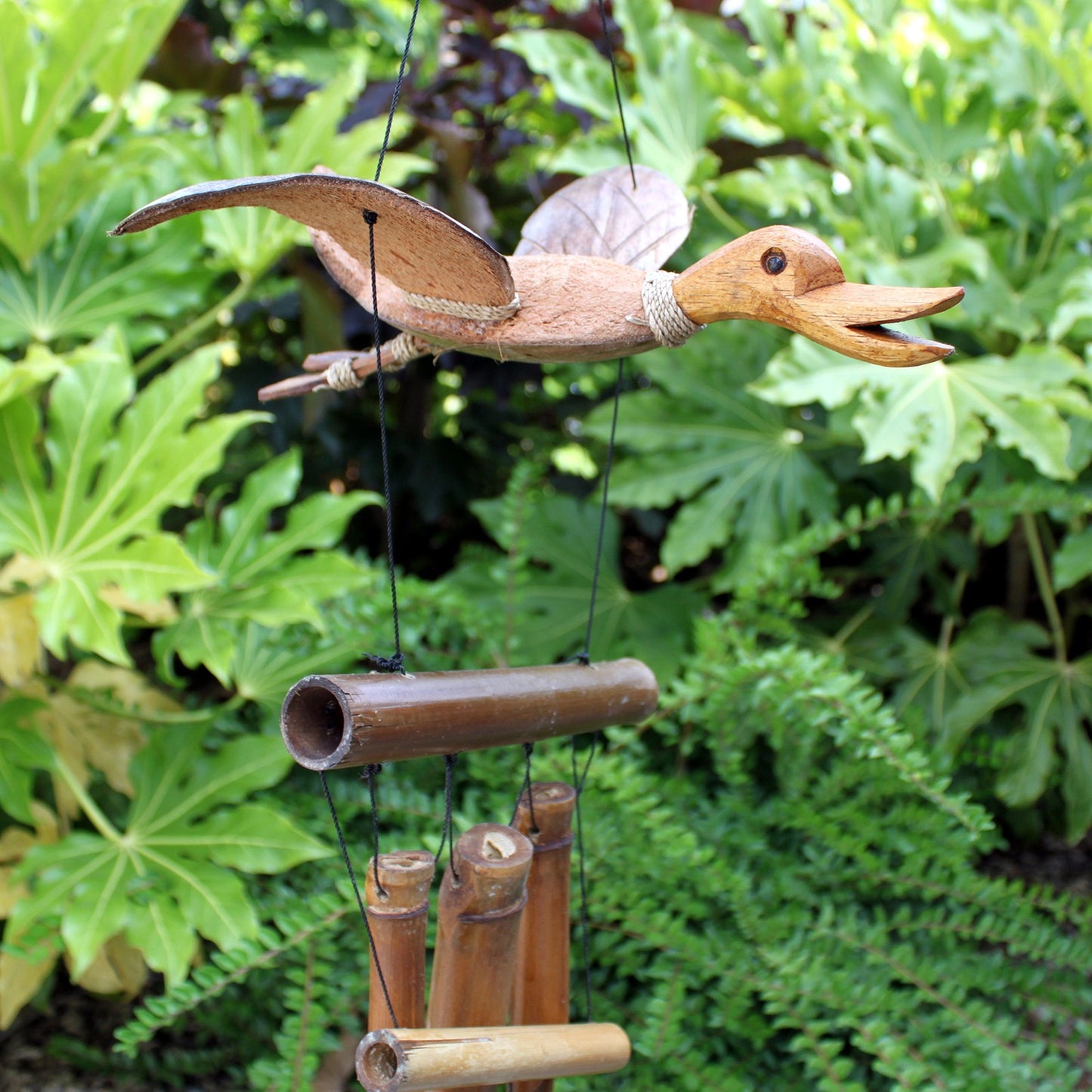 Handcrafted coconut and bamboo duck wind chime hanging in lush green garden, eco-friendly outdoor decor with natural tones