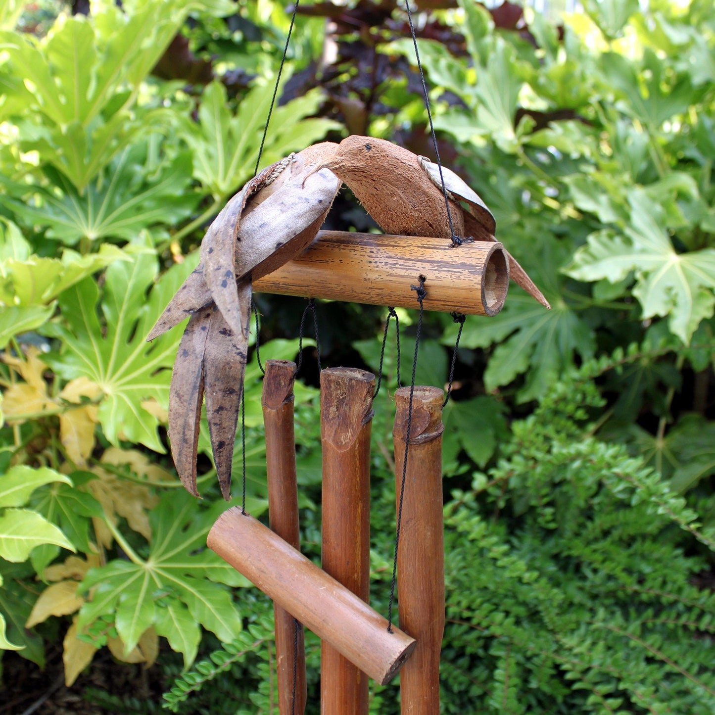 Eco-friendly twin bird wind chime hanging outdoors, made from coconut and bamboo, displayed among green foliage in a garden setting