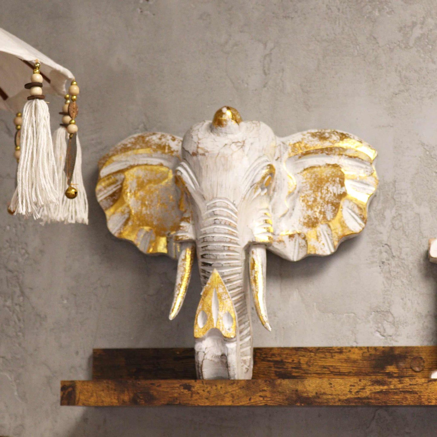 Gold and whitewash elephant head decor styled in modern interior on wooden shelf.